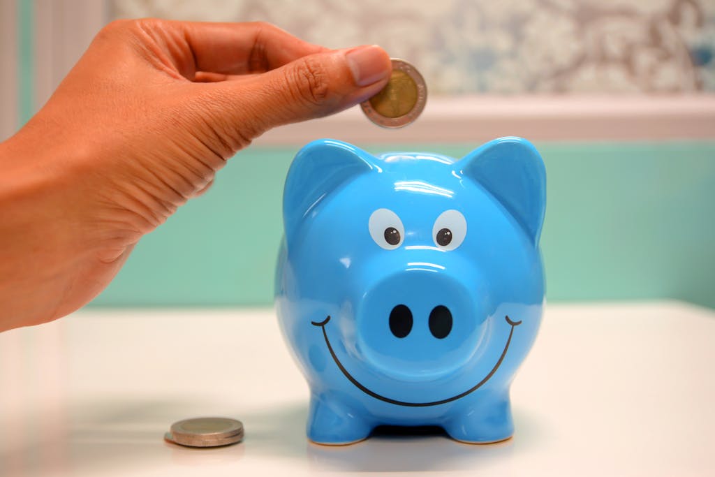 Mano insertando moneda en hucha azul para ahorro y gestión financiera